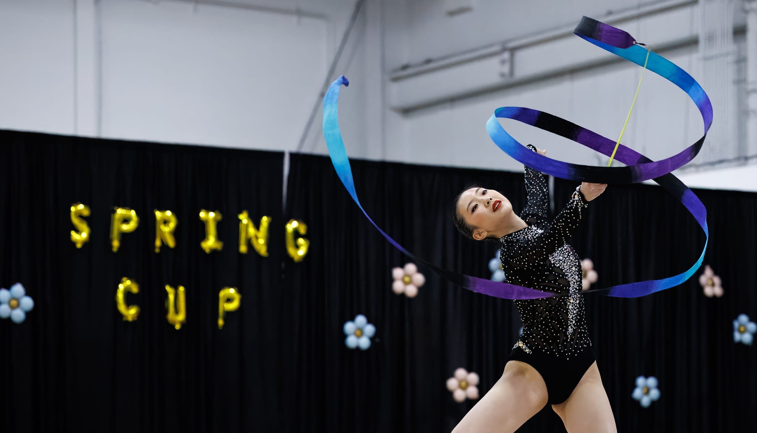 A Boston Rhythmic gymnast performing with a blue and purple ribbon at a Spring Cup event.
