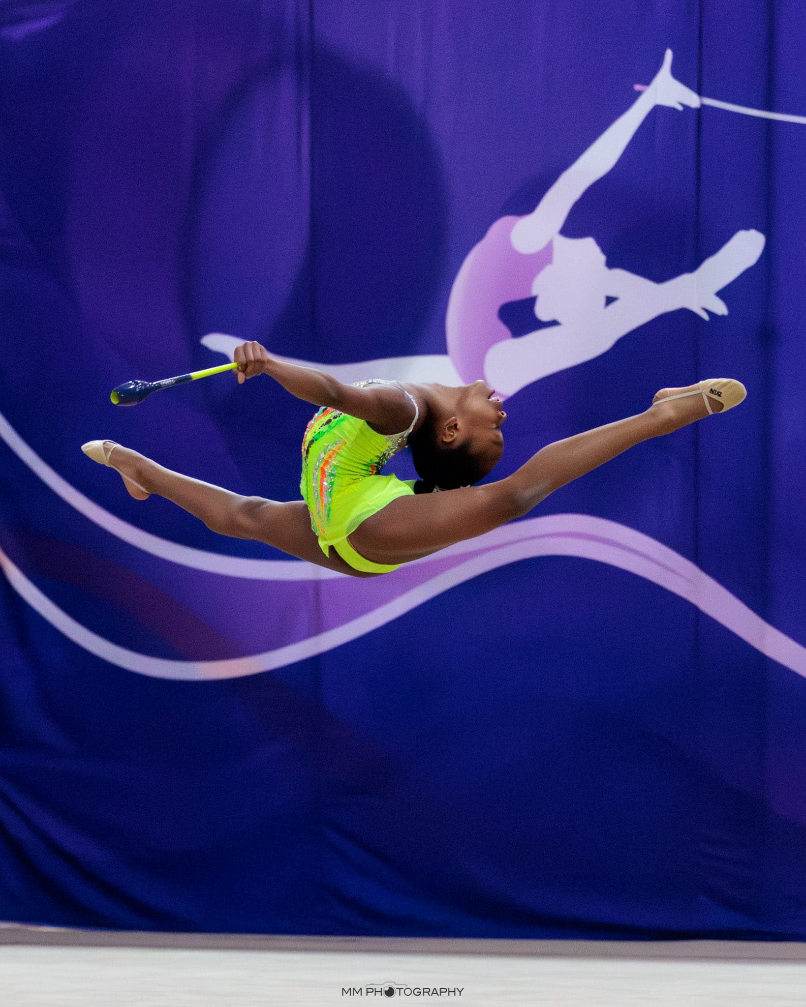 A gymnast in a full split leap holding clubs