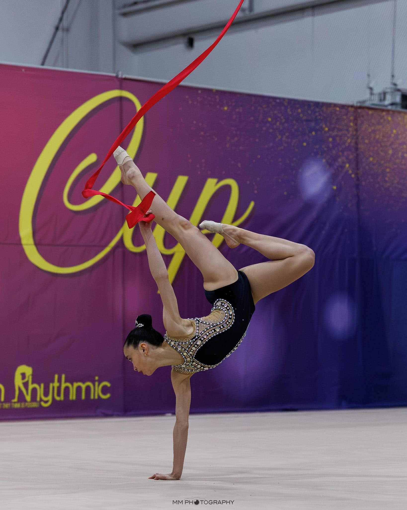 A gymnast in a one-hand backbend catching a red ribbon at Boston Cup