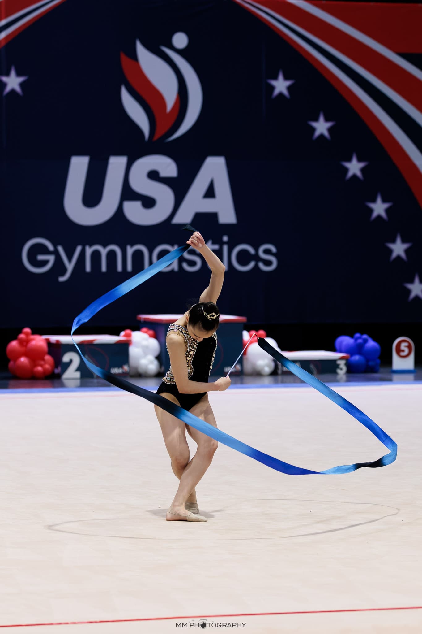 A gymnast spiraling a blue ribbon at a national competition
