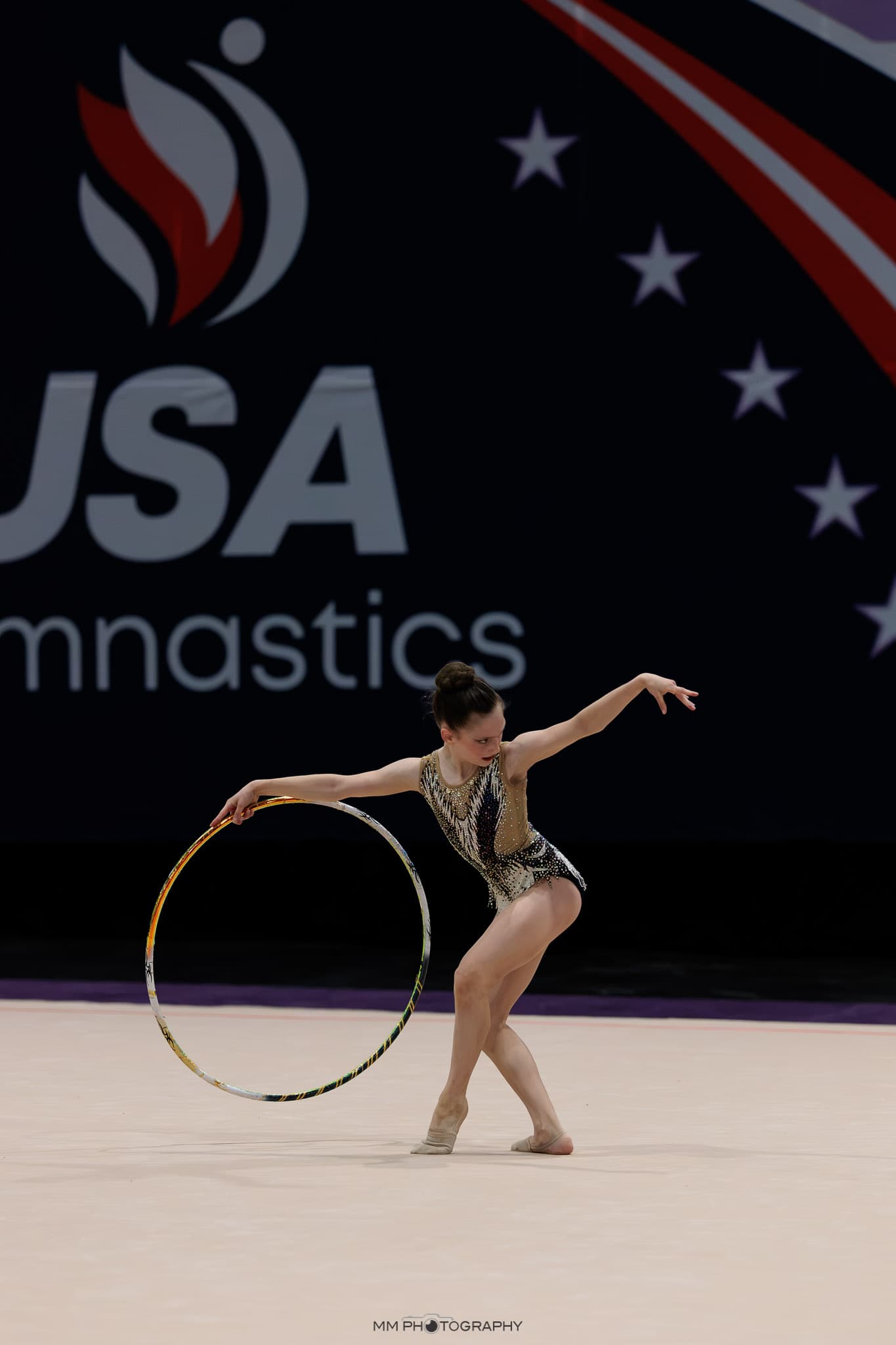 A gymnast posing with a hoop in front of a USA Gymnastics banner