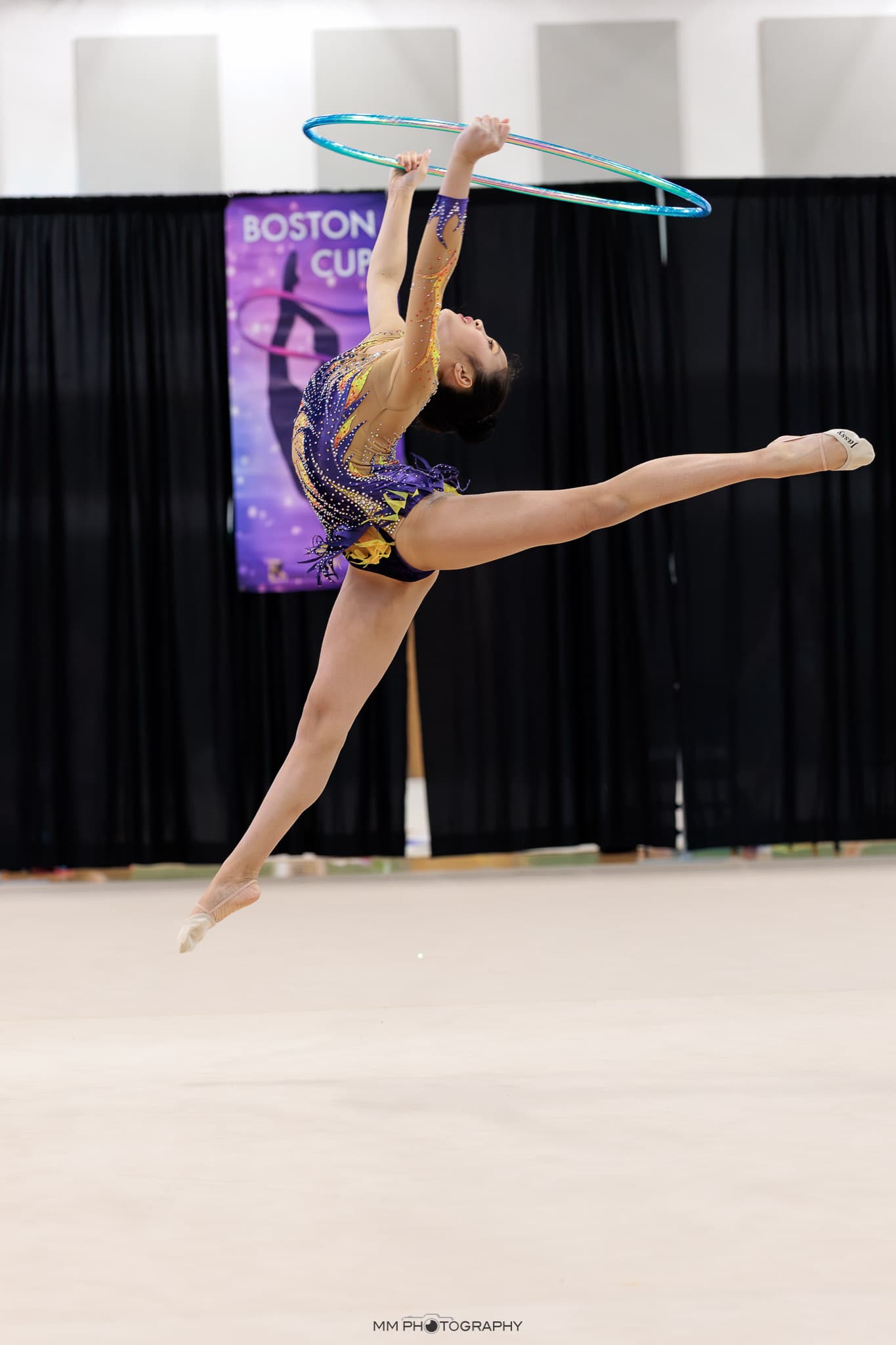 A gymnast in a split leap catching a hoop at Boston Cup