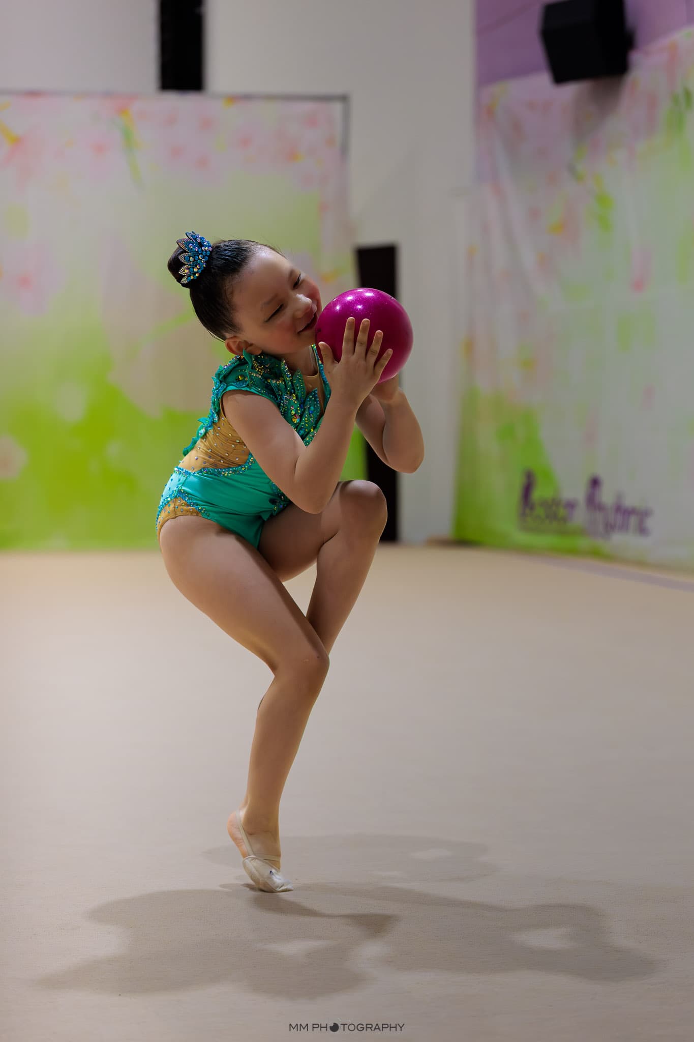 A young gymnast smiling while cradling a pink ball