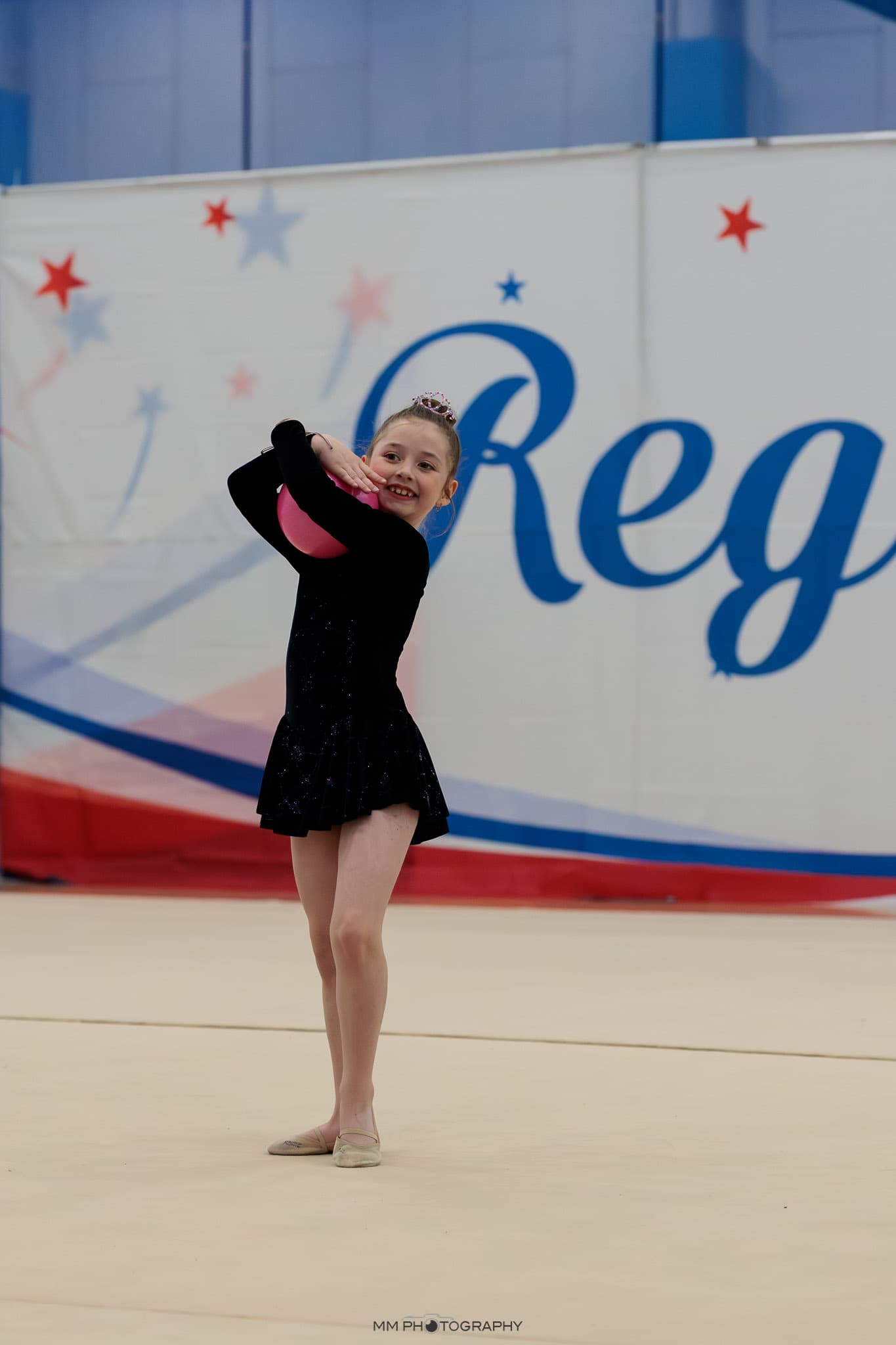 A smiling gymnast holding a pink ball behind her head