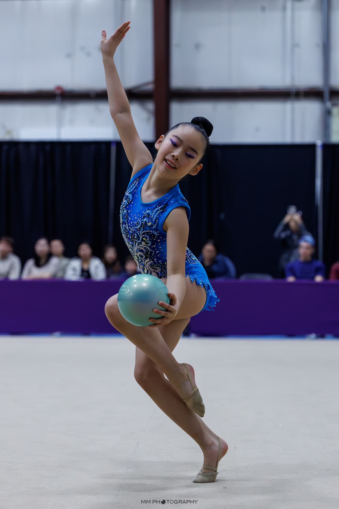 A gymnast holding a turquoise ball with an extended arm