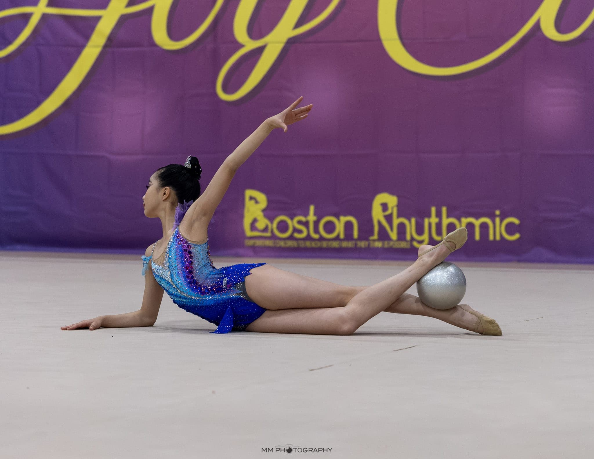 A gymnast in a reclining floor pose balancing a silver ball
