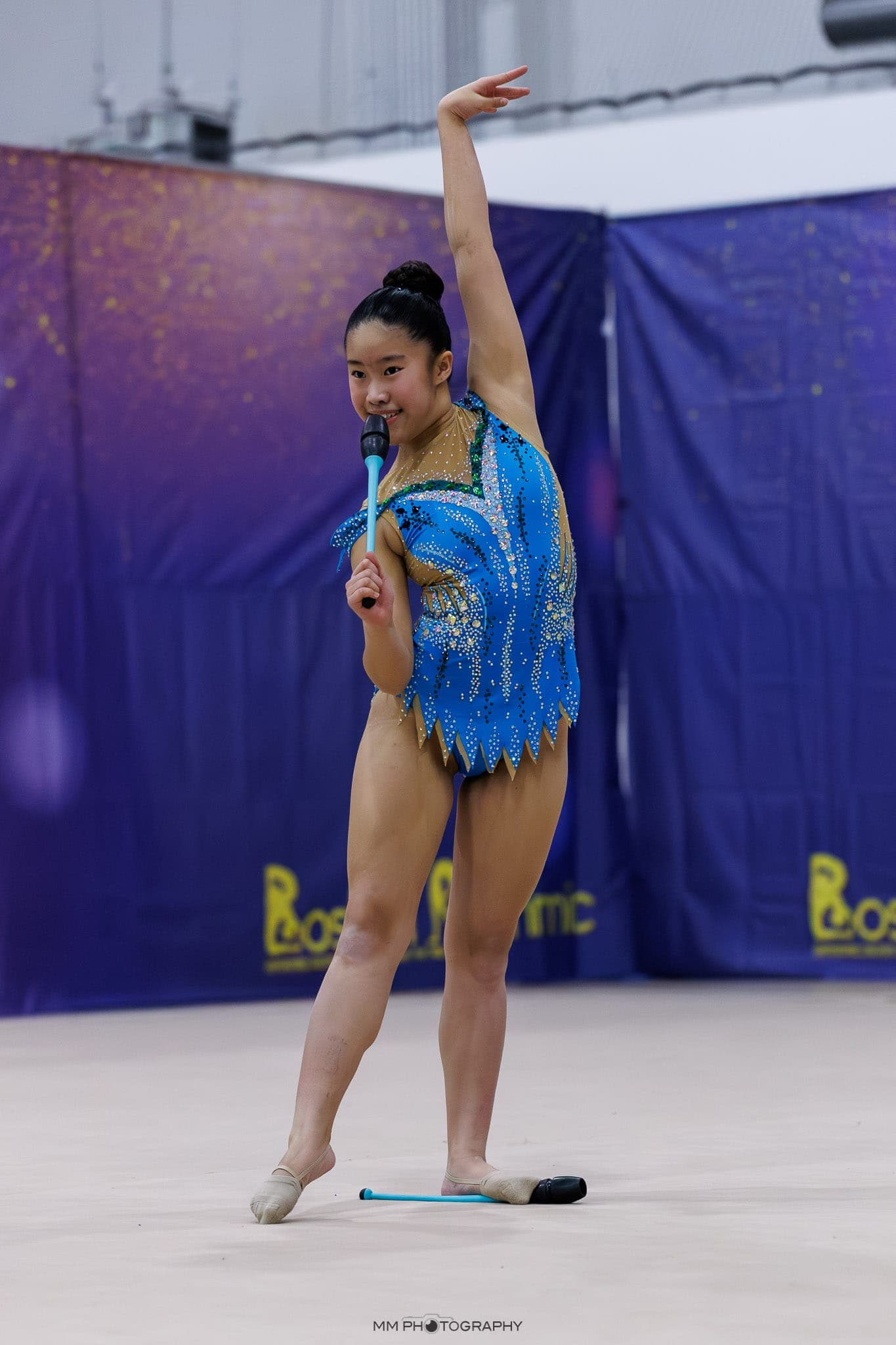 A gymnast in a blue leotard posing with clubs