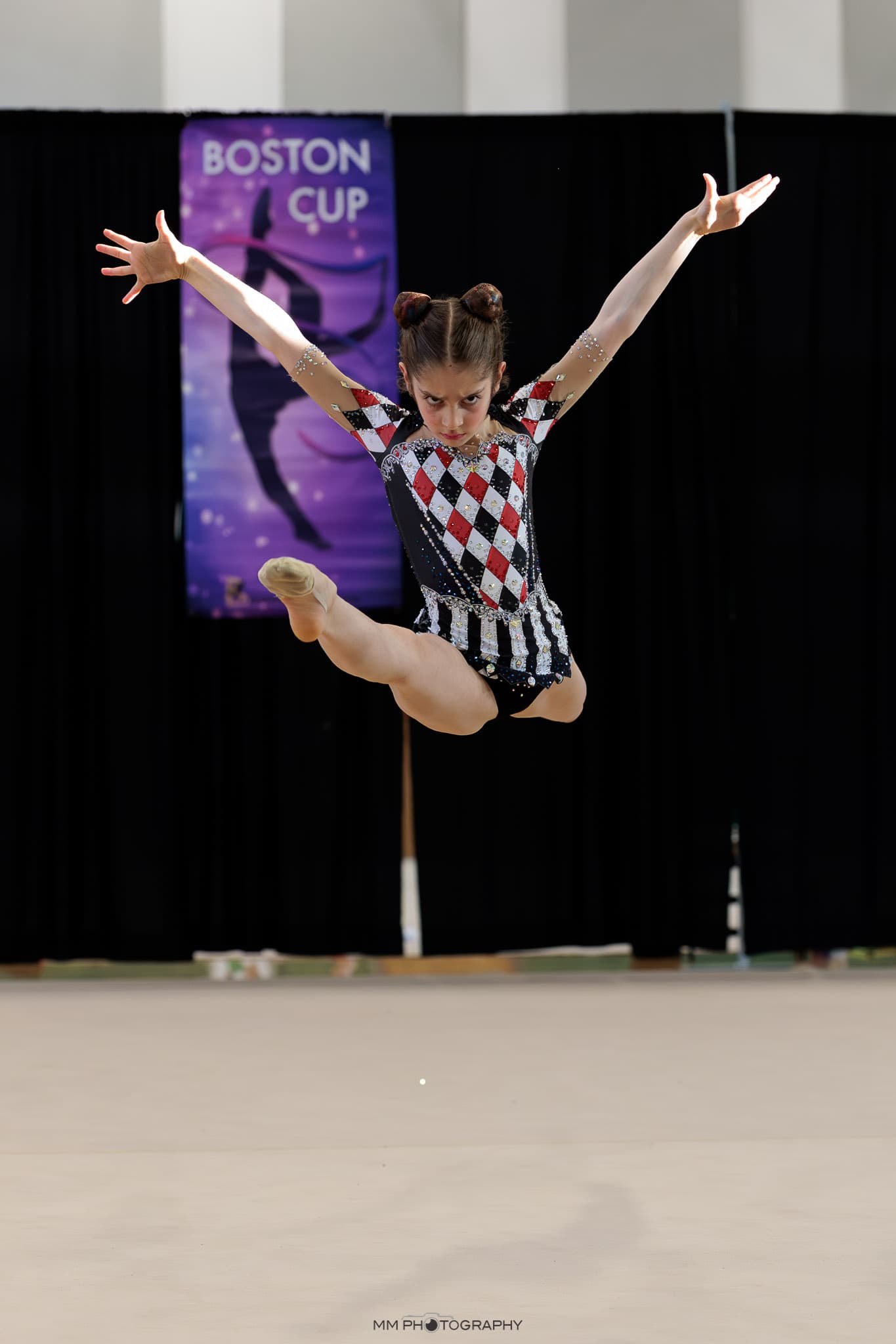 A gymnast in a harlequin leotard leaping at Boston Cup