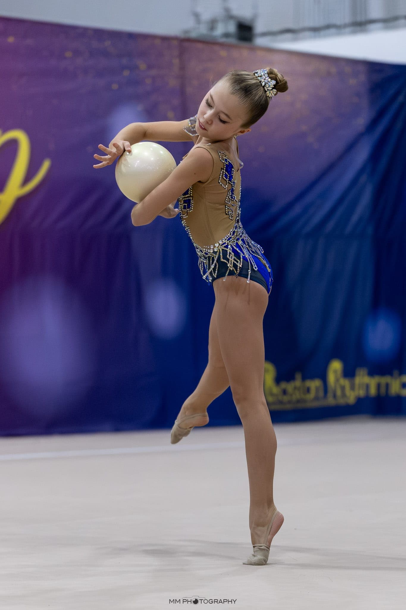 A young gymnast on relevé cradling a pearl-white ball