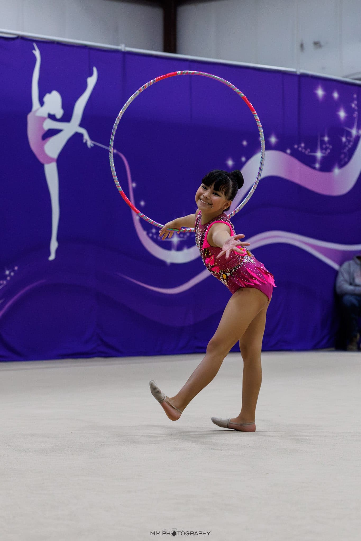 A smiling gymnast balancing a hoop mid-routine