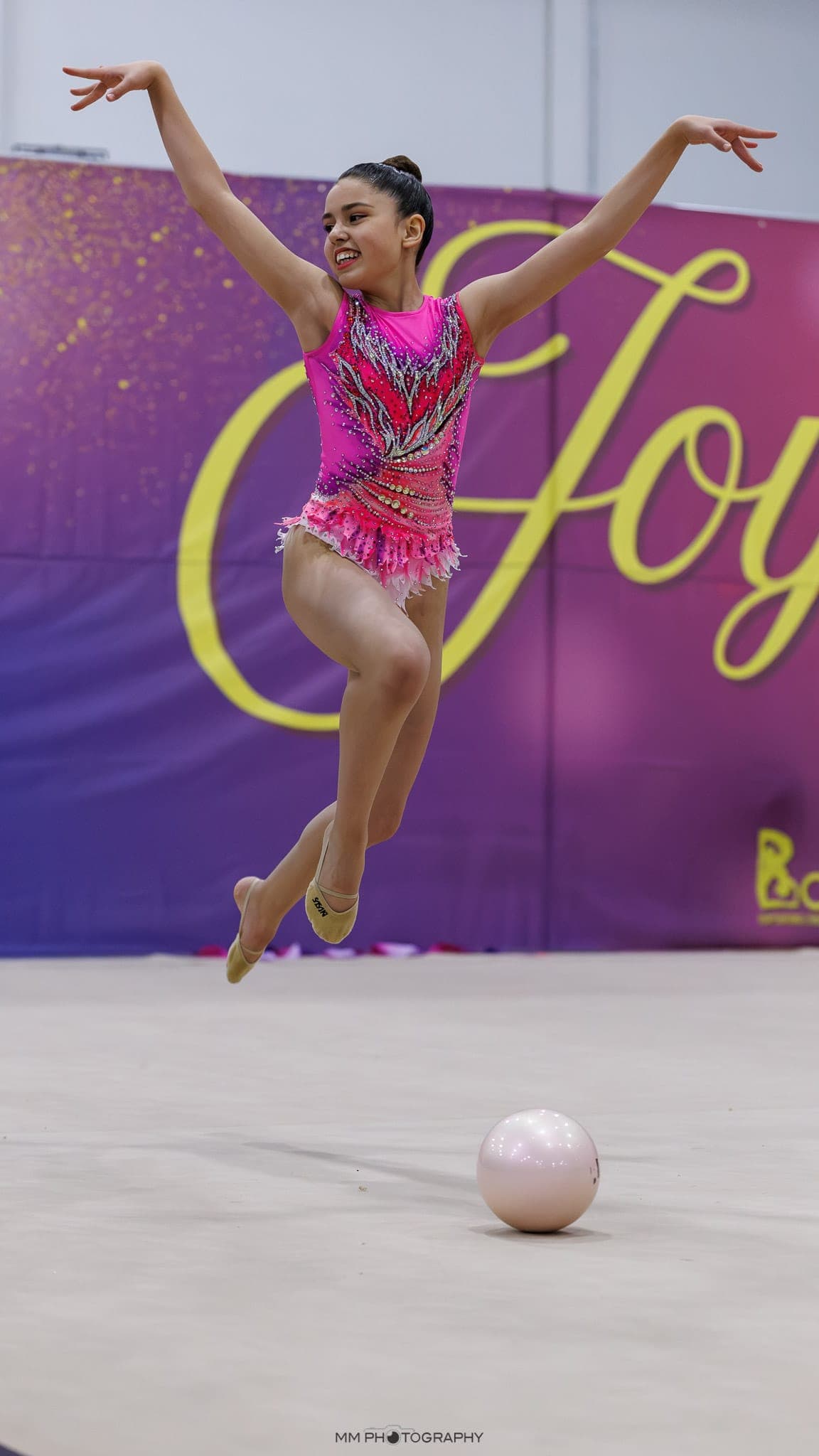 A gymnast leaping above a ball in a pink leotard
