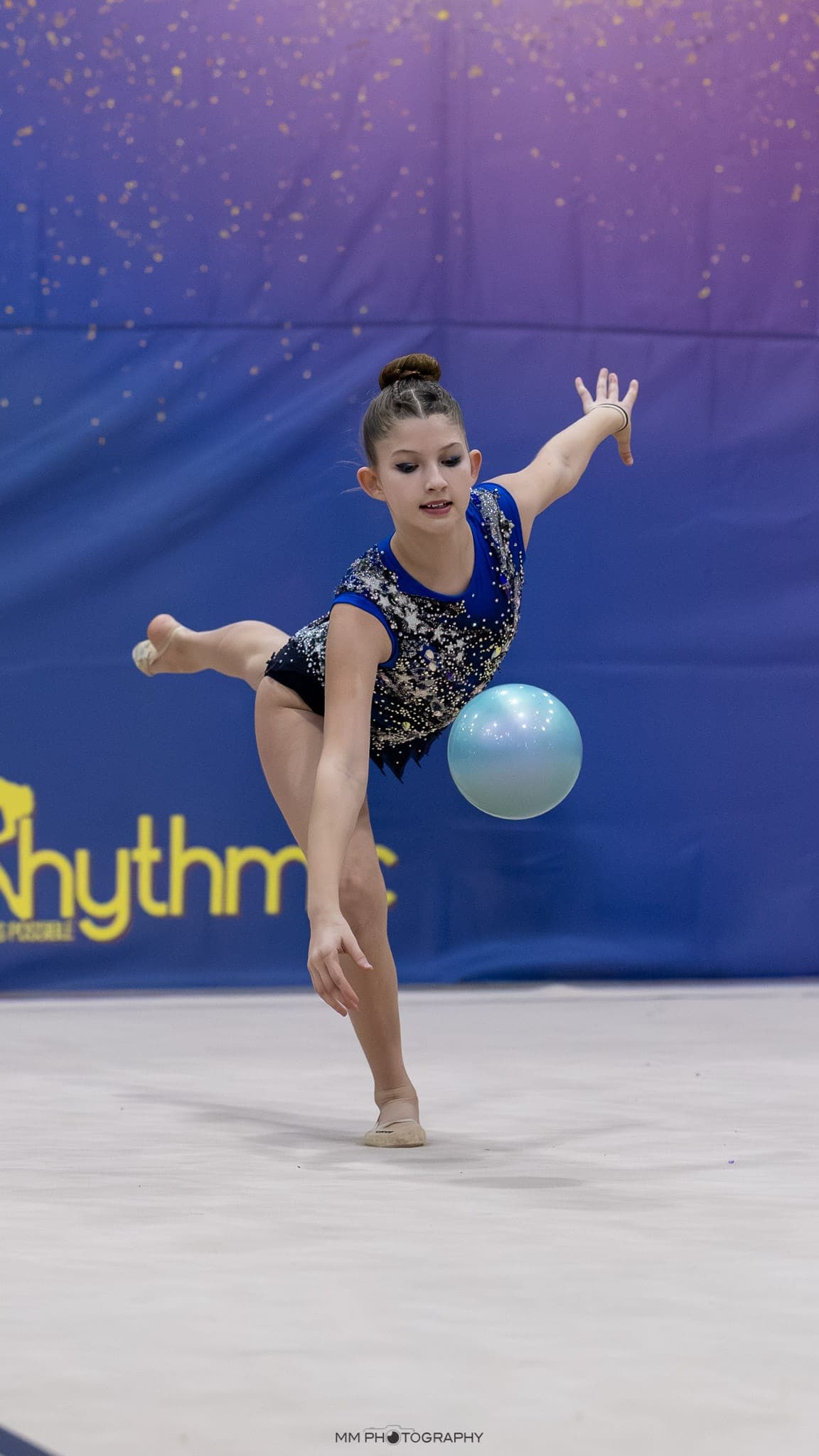 A gymnast reaching toward a ball during a routine