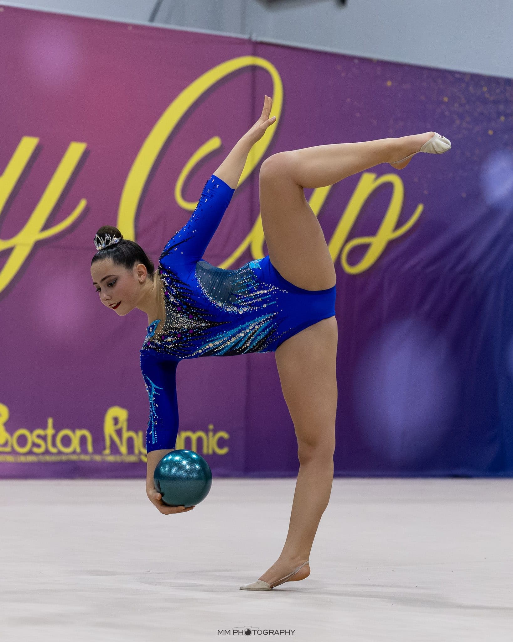 A gymnast in a standing split holding a teal ball at Boston Cup