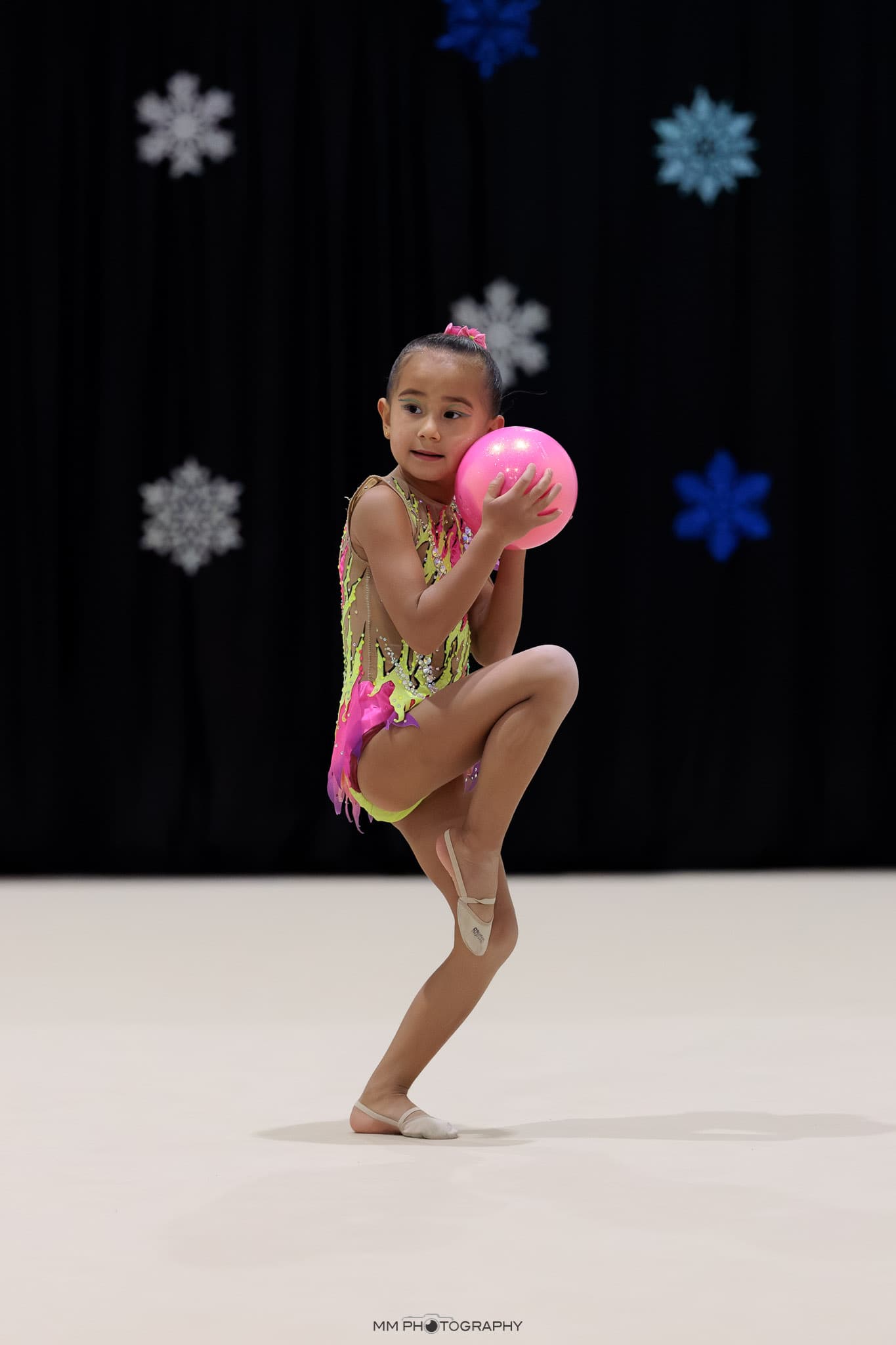 A young gymnast holding a pink ball against a snowflake backdrop