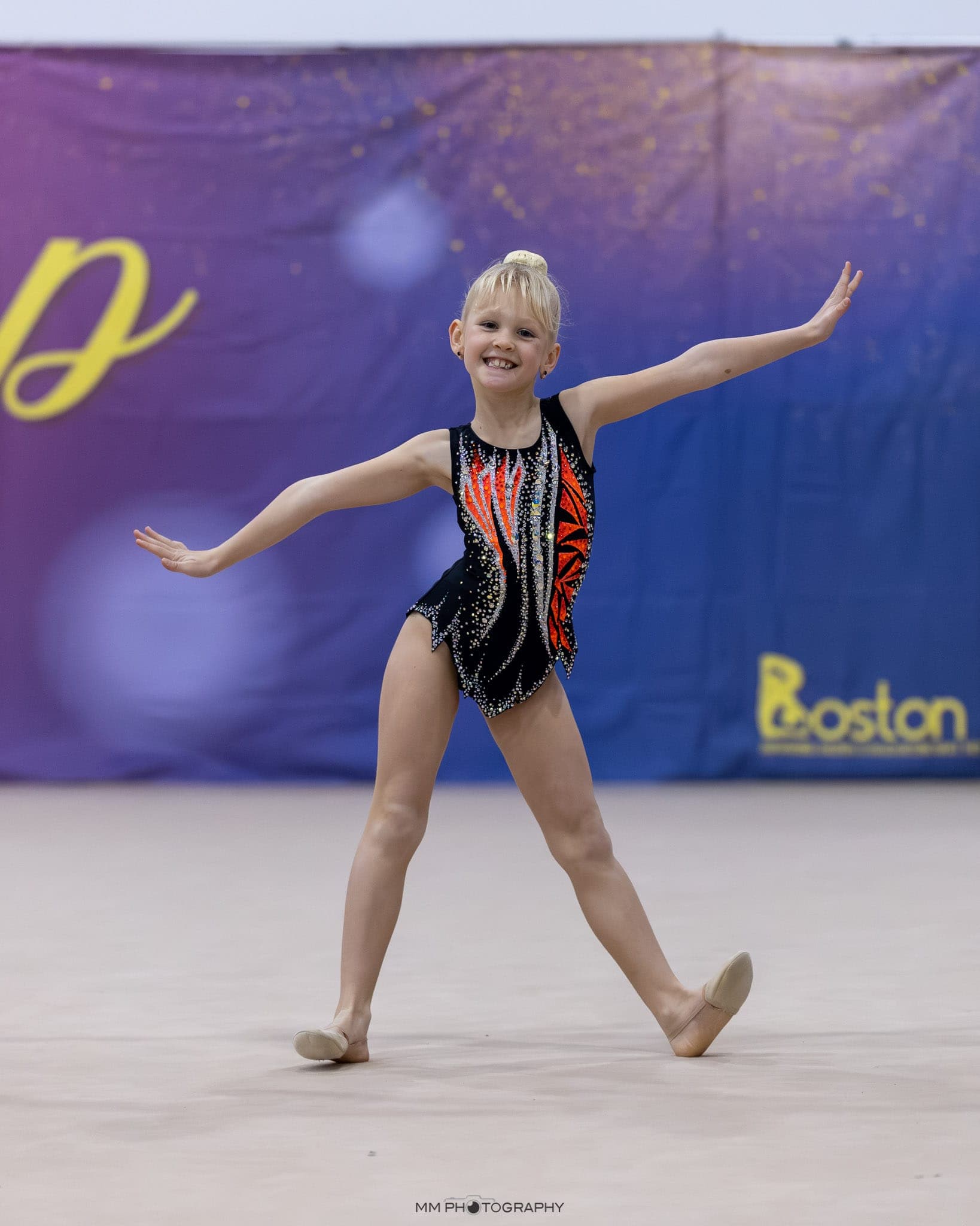 A young gymnast with arms outstretched during a floor routine