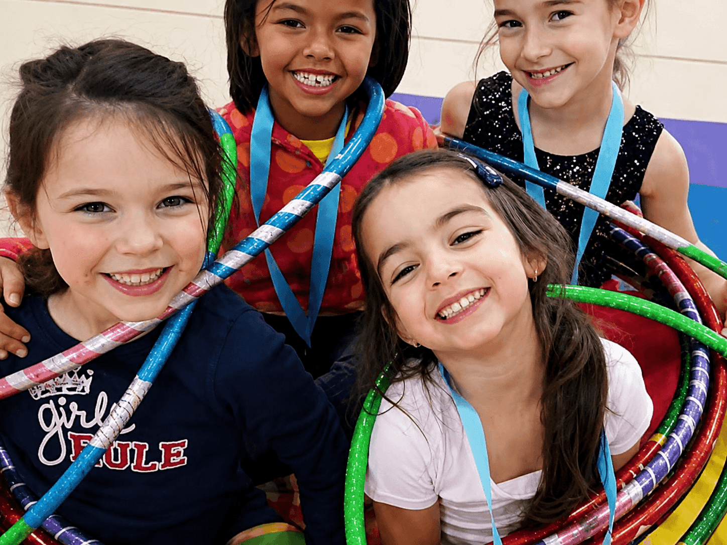 Four smiling young campers grouped together holding colorful gymnastics hoops